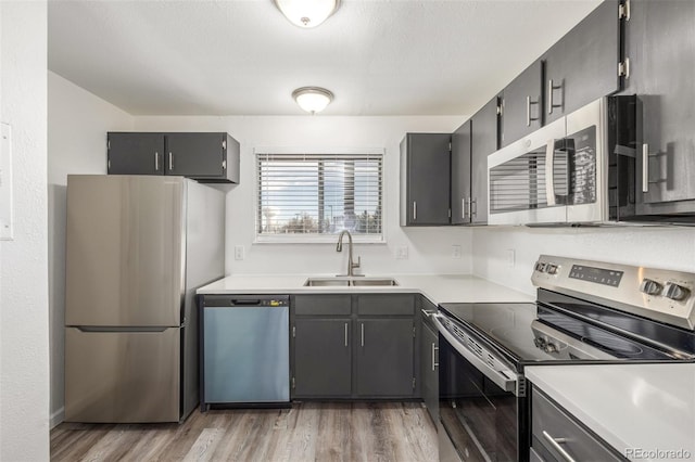 kitchen with appliances with stainless steel finishes, sink, light hardwood / wood-style flooring, and a textured ceiling