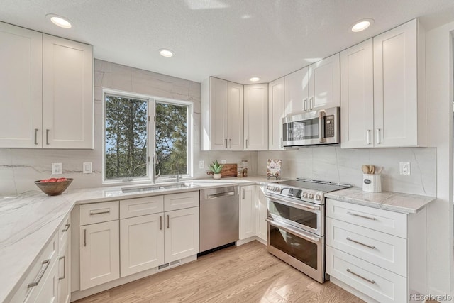 kitchen with decorative backsplash, appliances with stainless steel finishes, white cabinetry, and light hardwood / wood-style flooring