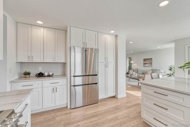 kitchen featuring light stone countertops, white cabinets, light wood-type flooring, and stainless steel fridge