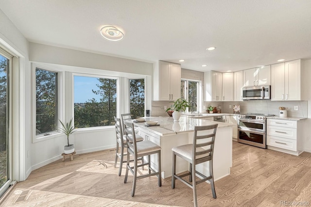 kitchen featuring white cabinets, stainless steel appliances, light hardwood / wood-style floors, a kitchen breakfast bar, and light stone counters