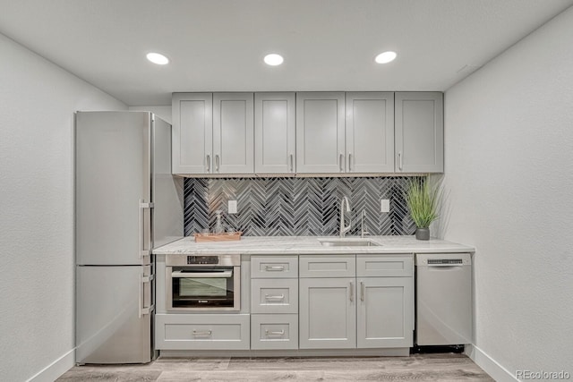 kitchen featuring light stone countertops, appliances with stainless steel finishes, decorative backsplash, sink, and light hardwood / wood-style floors