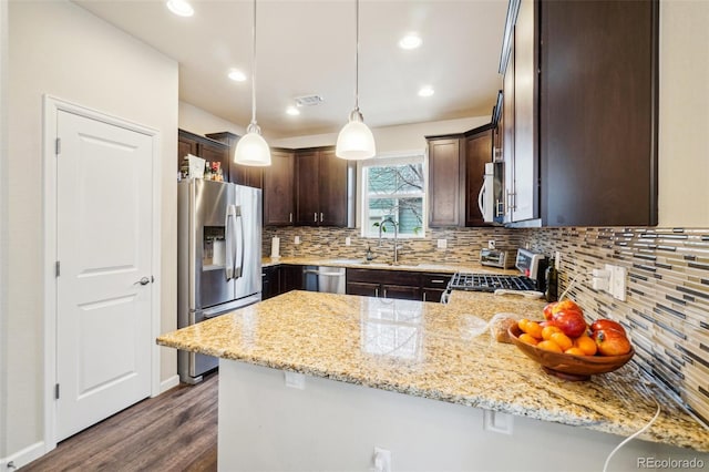 kitchen with dark brown cabinetry, appliances with stainless steel finishes, a peninsula, a sink, and backsplash