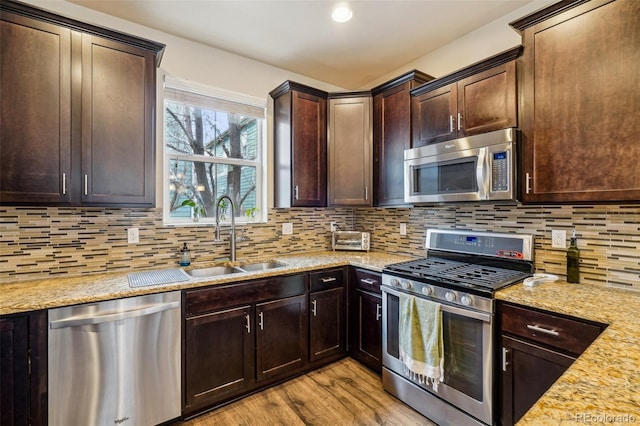 kitchen featuring tasteful backsplash, appliances with stainless steel finishes, light wood-style floors, a sink, and dark brown cabinets