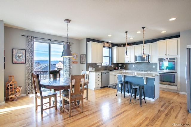 kitchen featuring stainless steel appliances, pendant lighting, light hardwood / wood-style flooring, white cabinets, and a kitchen island