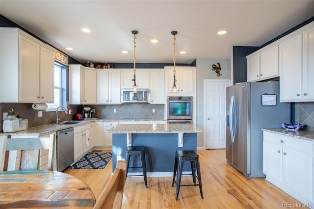 kitchen with sink, stainless steel appliances, light hardwood / wood-style flooring, pendant lighting, and a kitchen island