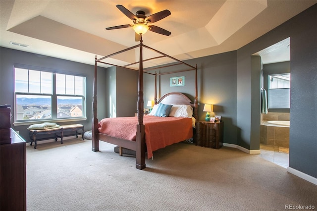 carpeted bedroom with ceiling fan, a tray ceiling, and ensuite bath