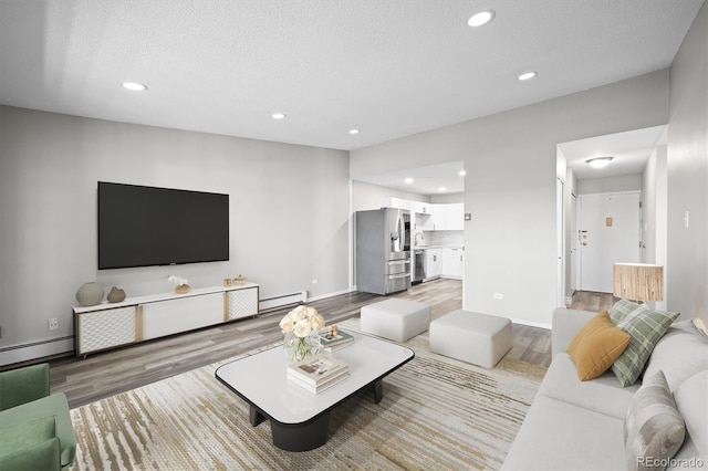 living area with light wood finished floors, baseboard heating, a textured ceiling, and recessed lighting