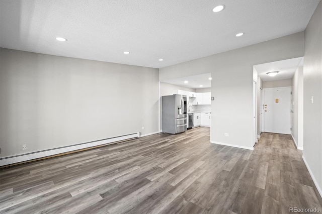 unfurnished living room featuring baseboards, a baseboard heating unit, and wood finished floors