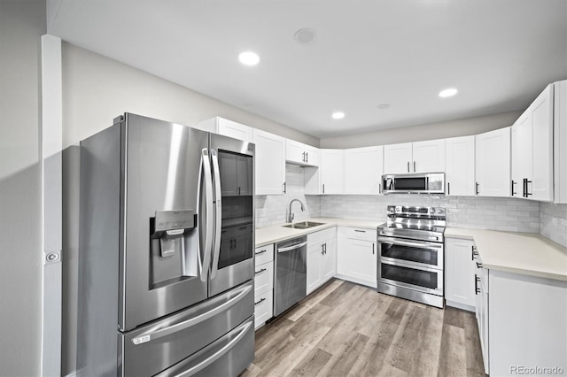 kitchen with appliances with stainless steel finishes, light wood-style floors, a sink, and backsplash