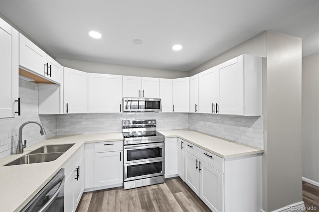 kitchen with stainless steel appliances, white cabinets, a sink, and wood finished floors