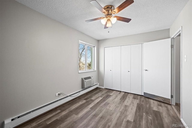 unfurnished bedroom featuring a textured ceiling, wood finished floors, a closet, baseboard heating, and a wall mounted AC