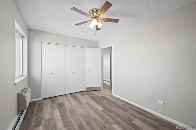 unfurnished bedroom with a textured ceiling, a baseboard radiator, wood finished floors, and baseboards