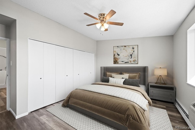 bedroom with a baseboard heating unit, a closet, a textured ceiling, and wood finished floors