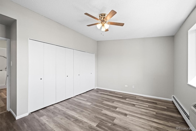 unfurnished bedroom featuring a textured ceiling, ceiling fan, a baseboard radiator, wood finished floors, and a closet