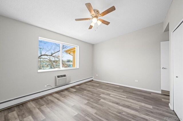 unfurnished bedroom with a textured ceiling, a baseboard radiator, wood finished floors, baseboards, and an AC wall unit