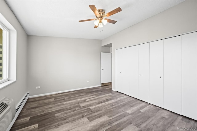 unfurnished bedroom with baseboards, ceiling fan, wood finished floors, an AC wall unit, and a closet