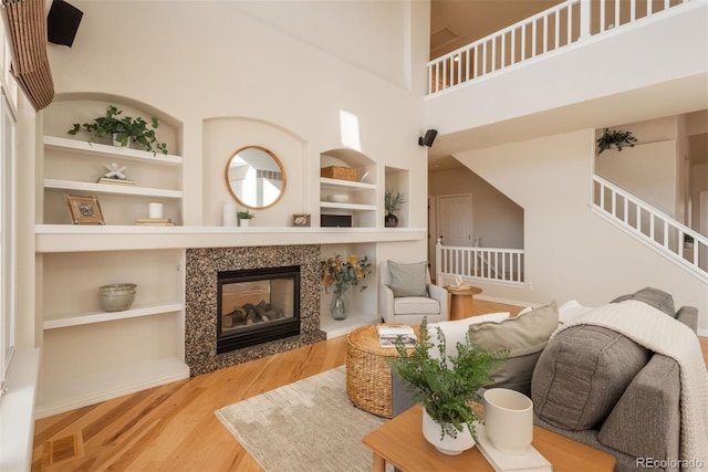 living room featuring hardwood / wood-style flooring, a tiled fireplace, built in shelves, and a high ceiling