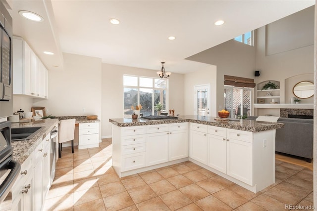 kitchen featuring stone countertops, a chandelier, stainless steel dishwasher, kitchen peninsula, and white cabinets