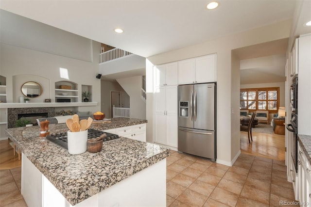 kitchen with stainless steel appliances, a kitchen island, white cabinets, and stone counters