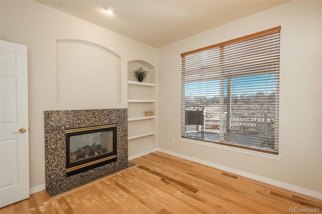 unfurnished living room with hardwood / wood-style flooring, a high end fireplace, and built in features