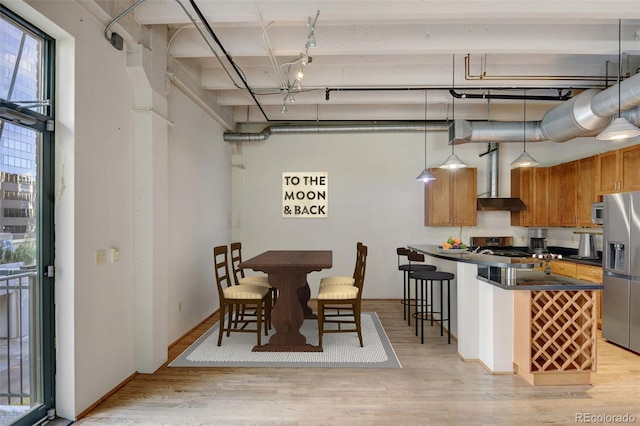 kitchen with wall chimney exhaust hood, light wood-type flooring, dark countertops, brown cabinetry, and stainless steel appliances