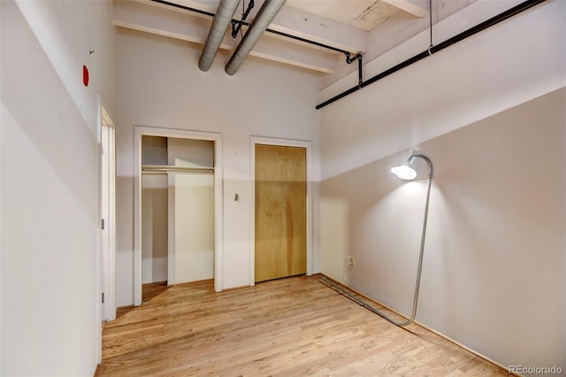 unfurnished bedroom featuring light wood-style flooring, a high ceiling, and two closets