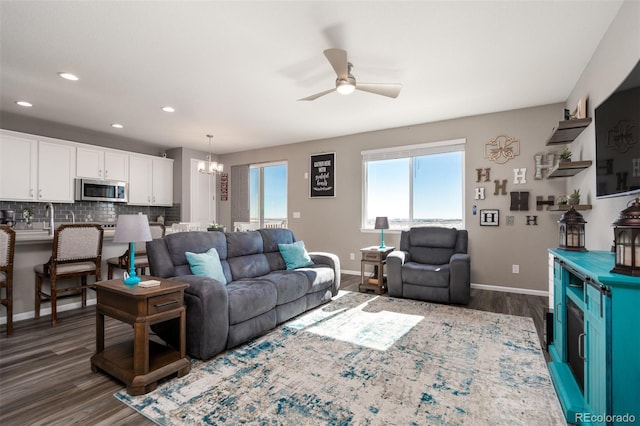 living room featuring ceiling fan with notable chandelier, dark wood-type flooring, and sink