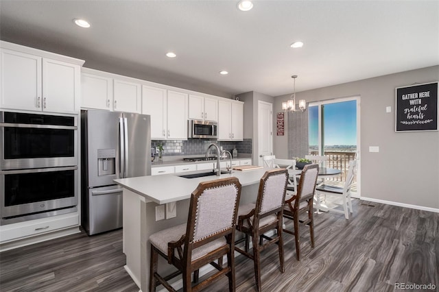 kitchen featuring stainless steel appliances, pendant lighting, dark hardwood / wood-style floors, white cabinetry, and an island with sink