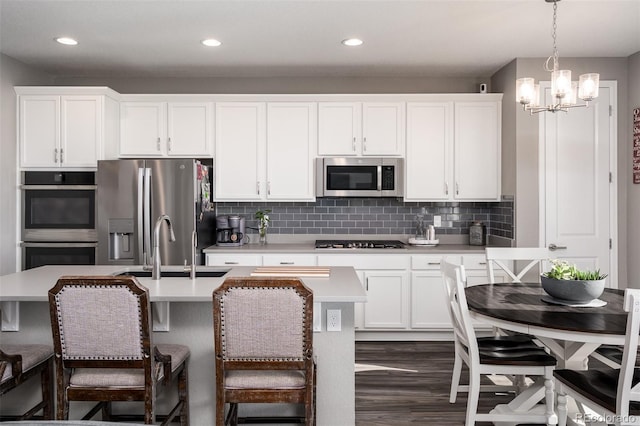 kitchen featuring stainless steel appliances, an inviting chandelier, an island with sink, decorative light fixtures, and white cabinets