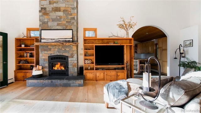 13416 Kuehster Rd, Littleton, CO 80127 - living room featuring wood finished floors, a stone fireplace, arched walkways, and baseboard heating