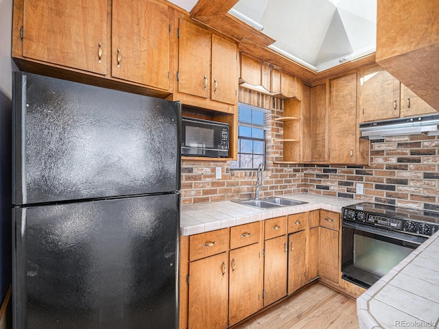 kitchen with sink, light hardwood / wood-style flooring, tile counters, decorative backsplash, and black appliances