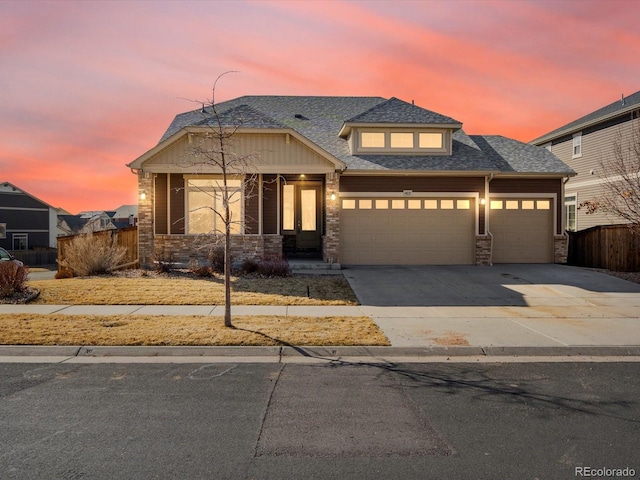 view of front of home with a garage, fence, driveway, stone siding, and roof with shingles