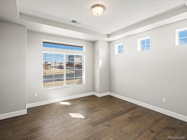 empty room featuring dark wood-type flooring, visible vents, and baseboards