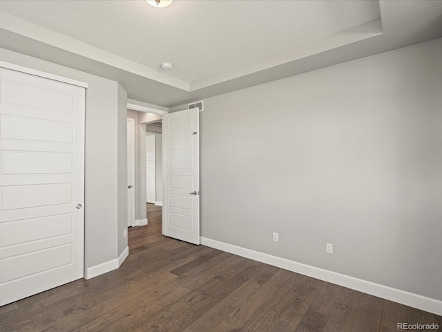 unfurnished bedroom with dark wood-style floors, a raised ceiling, visible vents, and baseboards