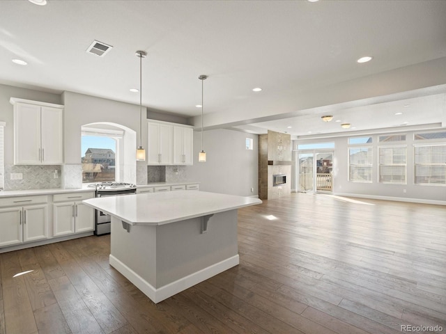 kitchen featuring stainless steel range with gas cooktop, visible vents, open floor plan, and dark wood finished floors