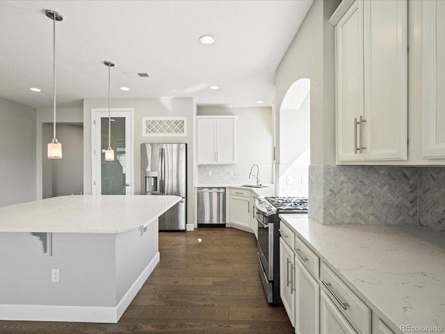 kitchen with light stone counters, dark wood-style flooring, appliances with stainless steel finishes, white cabinetry, and a sink