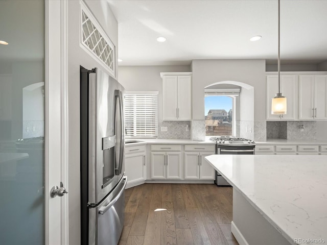 kitchen with dark wood-style flooring, white cabinetry, appliances with stainless steel finishes, decorative backsplash, and light stone countertops