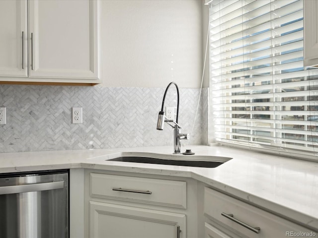 kitchen with dishwasher, tasteful backsplash, a sink, and white cabinetry