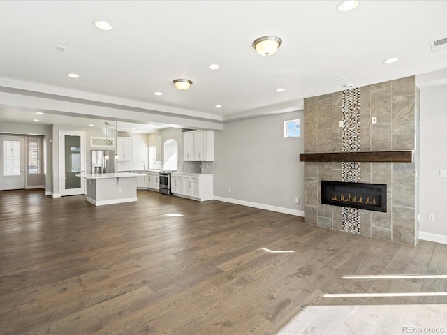 unfurnished living room featuring baseboards, dark wood-type flooring, a fireplace, and recessed lighting