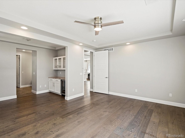 spare room featuring visible vents, dark wood-type flooring, a ceiling fan, a bar, and baseboards