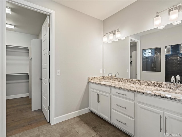 bathroom featuring a sink, a spacious closet, baseboards, and double vanity