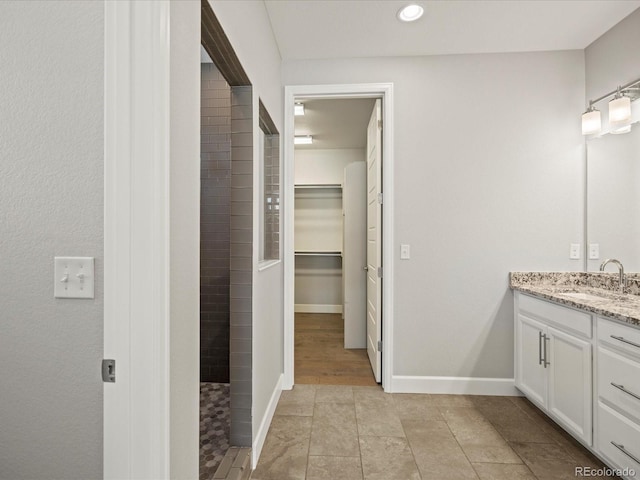 bathroom with baseboards, a spacious closet, a tile shower, vanity, and recessed lighting