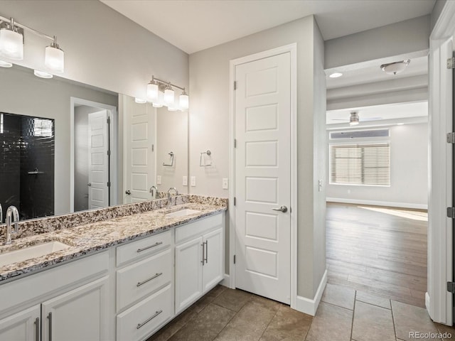 full bath featuring double vanity, a sink, a ceiling fan, and baseboards