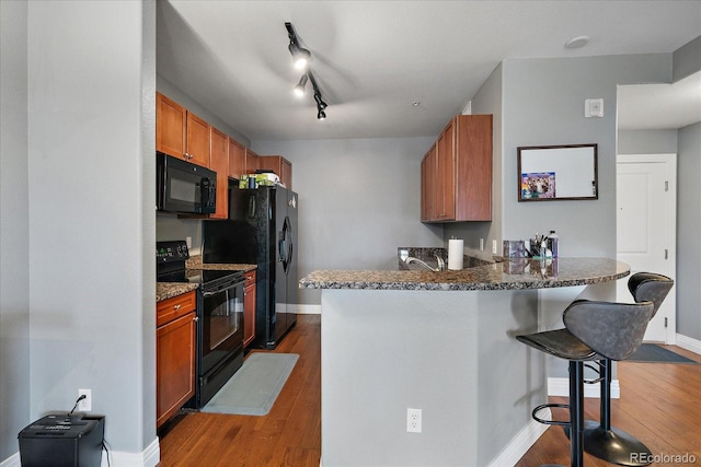 kitchen featuring a breakfast bar, black appliances, rail lighting, kitchen peninsula, and dark wood-type flooring