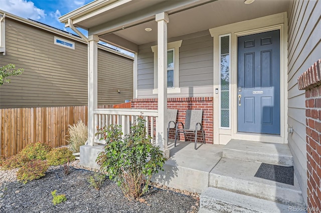 property entrance featuring brick siding, covered porch, and fence