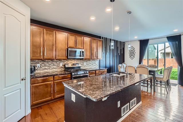 kitchen featuring stainless steel appliances, a sink, brown cabinets, dark wood-style flooring, and backsplash