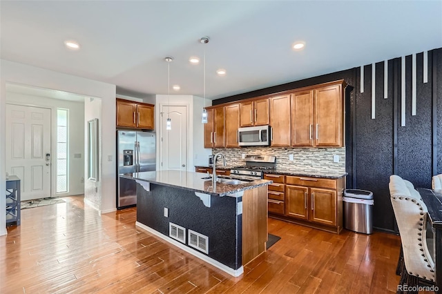 kitchen with appliances with stainless steel finishes, brown cabinetry, a sink, dark wood finished floors, and backsplash