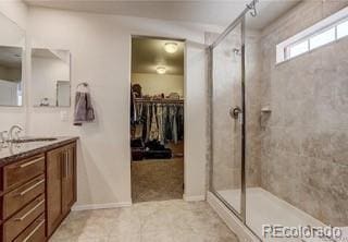 bathroom with a stall shower, vanity, a walk in closet, and tile patterned floors