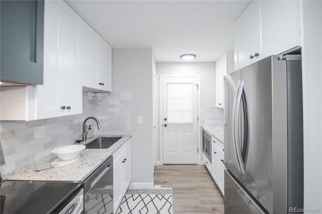 kitchen featuring white cabinetry, sink, light stone counters, light hardwood / wood-style floors, and appliances with stainless steel finishes