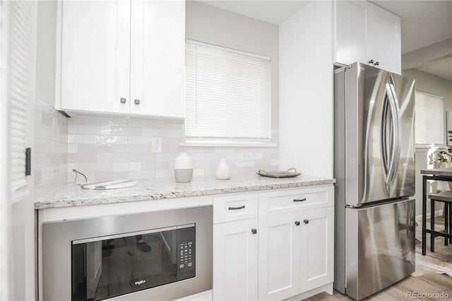 kitchen featuring white cabinets, light wood-type flooring, stainless steel refrigerator, and light stone counters